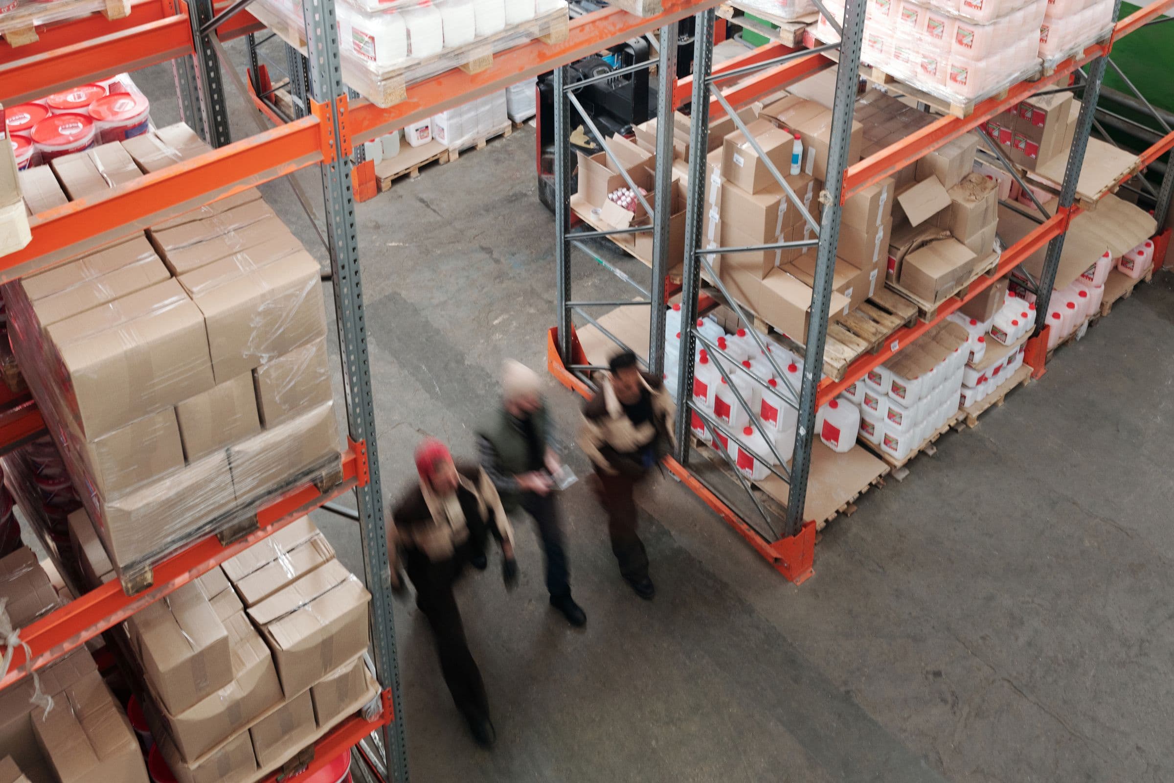 Warehouse staff crossing the floor of a distribution centre, cased goods and shrink-wrapped pallets racked on both sides