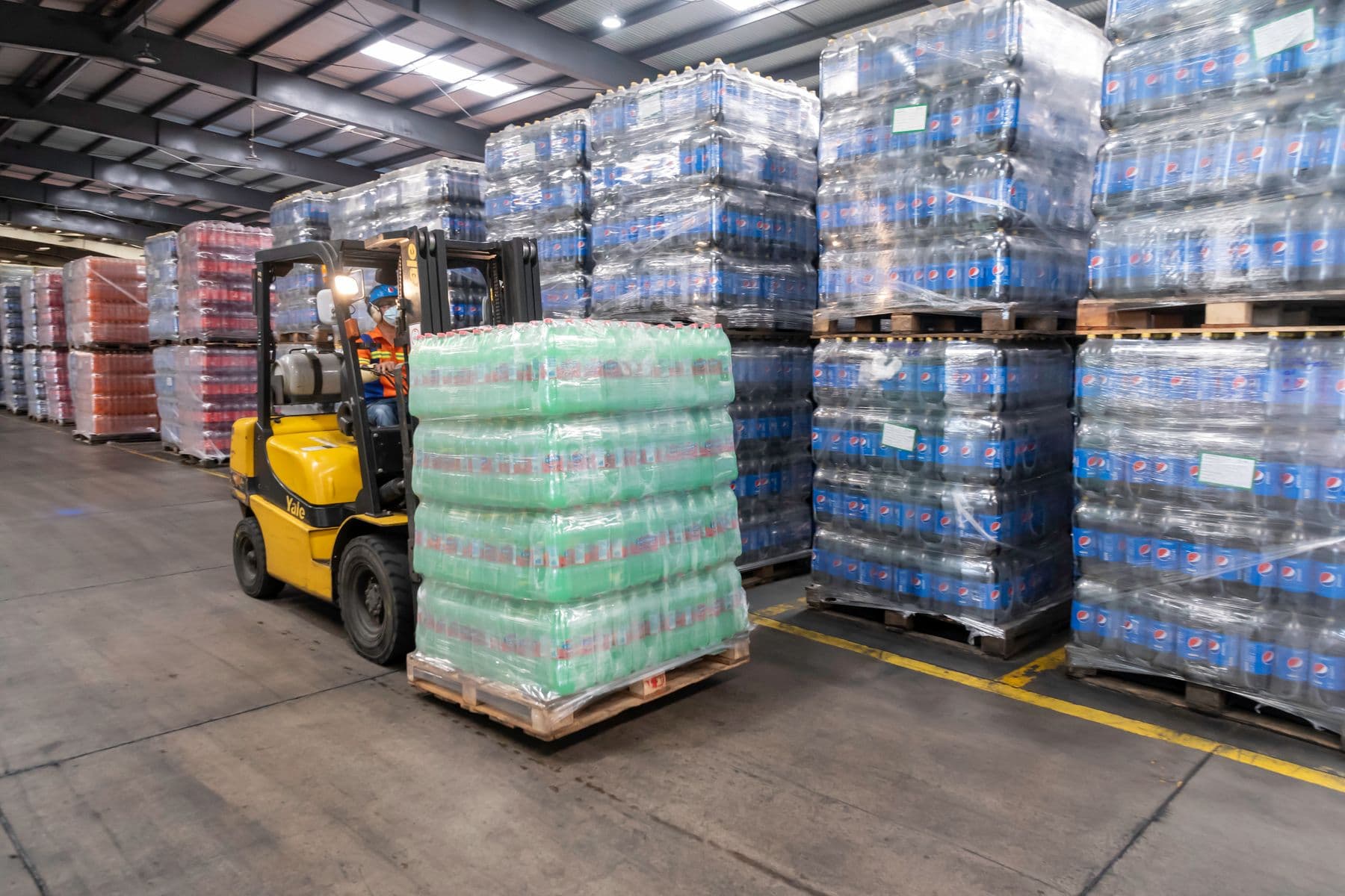 A forklift carrying a pallet of cased drinks past stacked pallets of bottled water