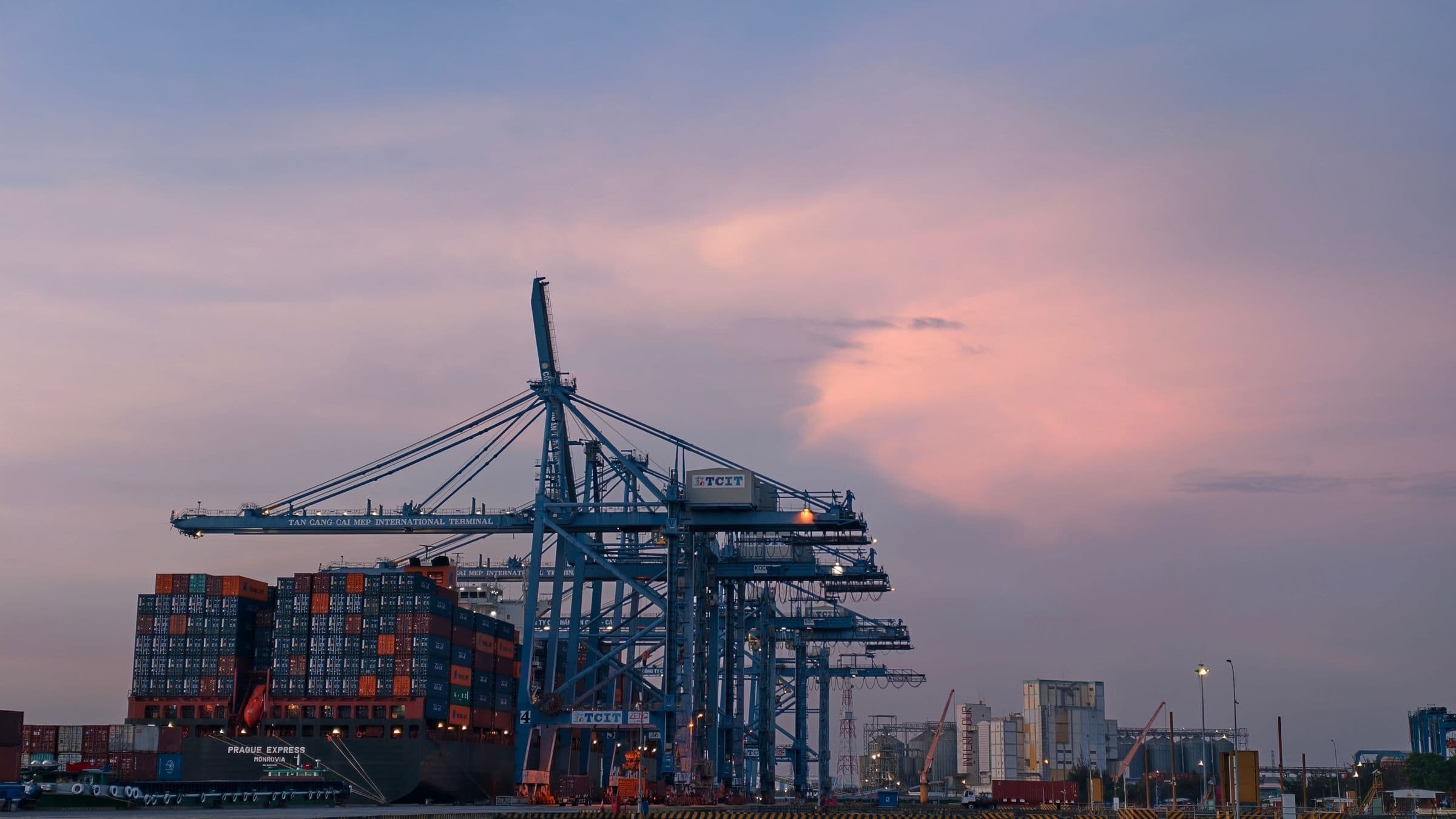 A container ship under gantry cranes at a Vietnamese terminal at dusk