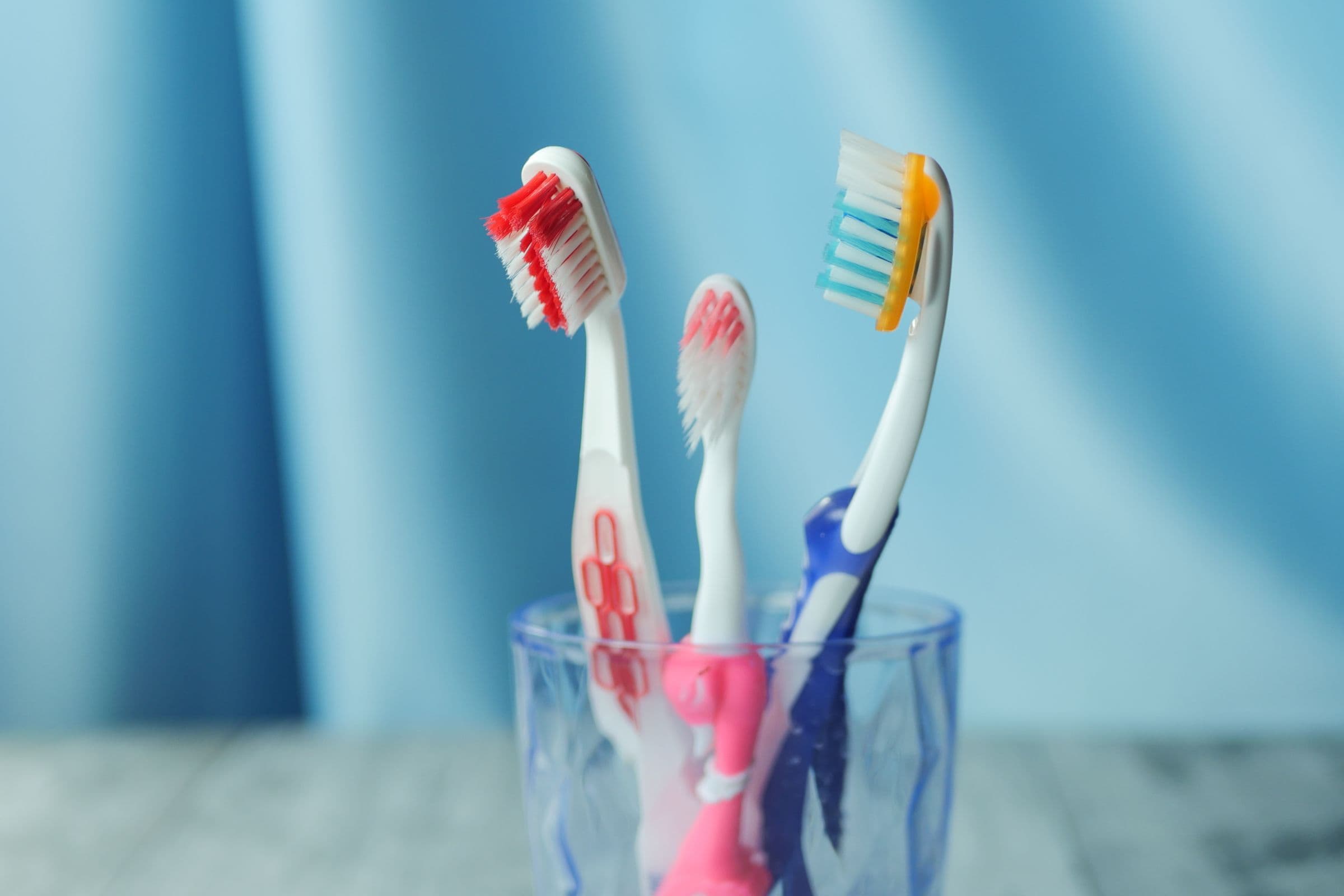 Three toothbrushes standing in a glass against a blue background.