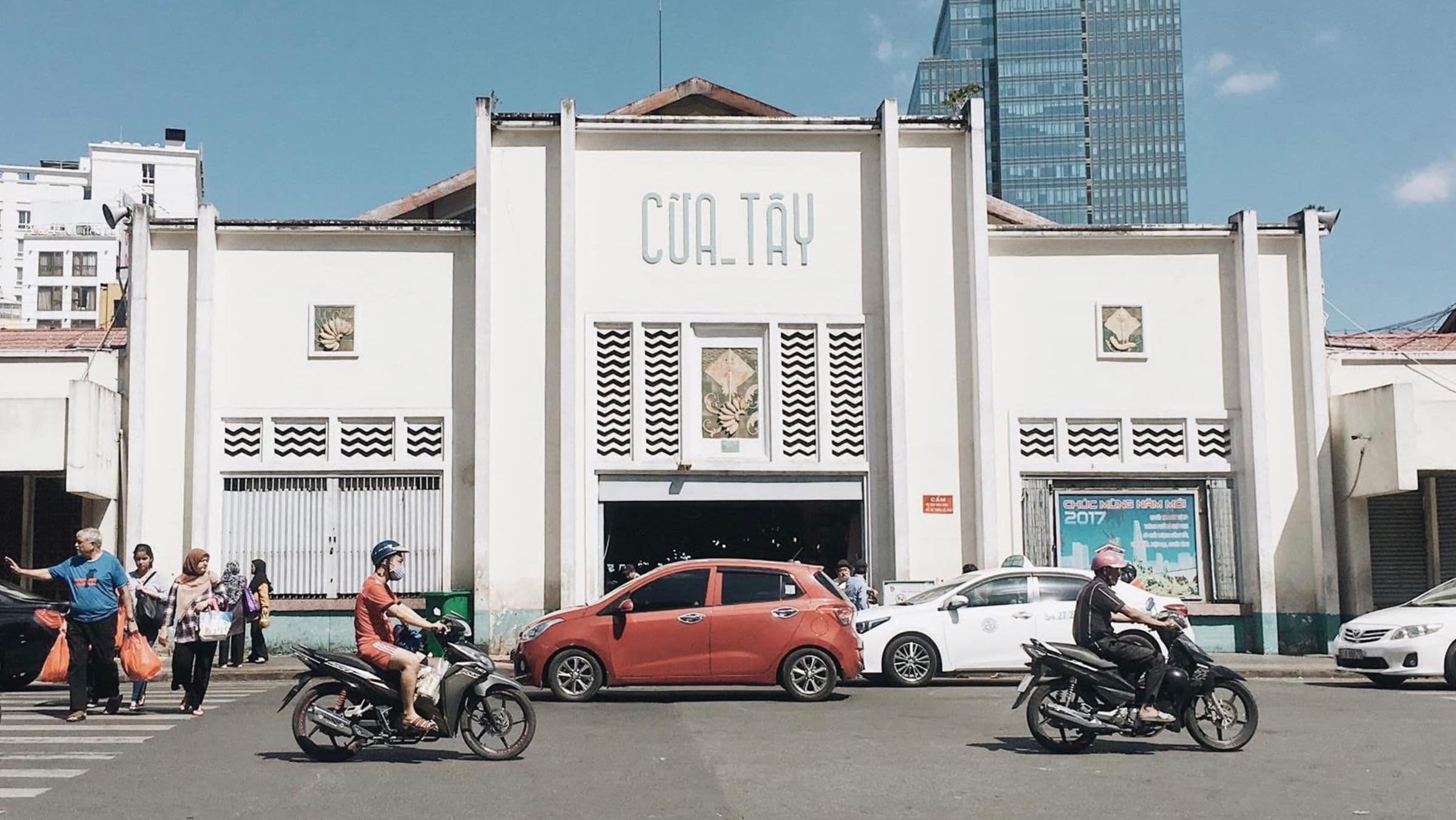 The west entrance of Ben Thanh Market in Ho Chi Minh City, motorbikes and shoppers crossing in front of it