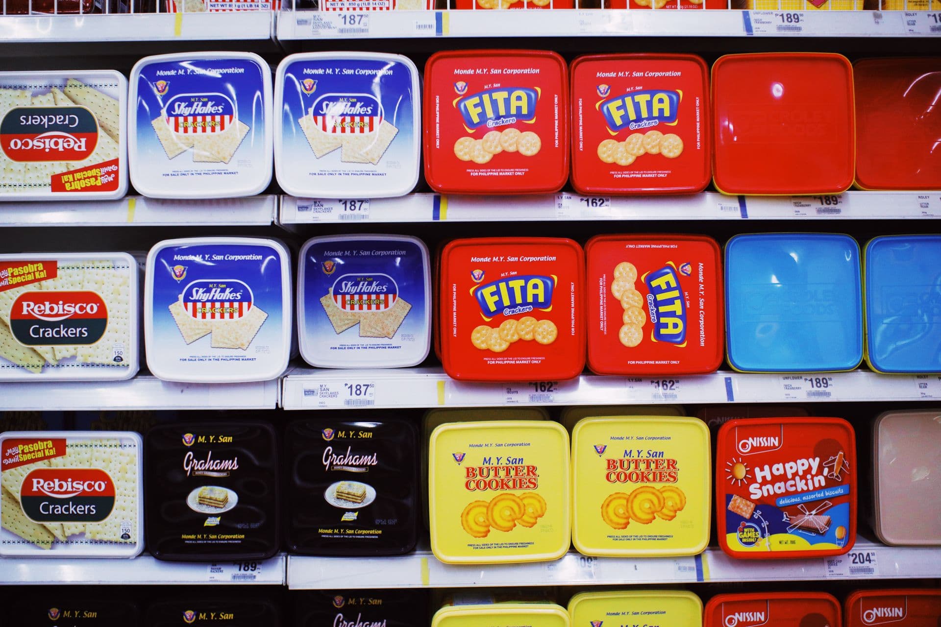 Assorted colorful boxes of sweet cookies placed on shelves with prices in a supermarket