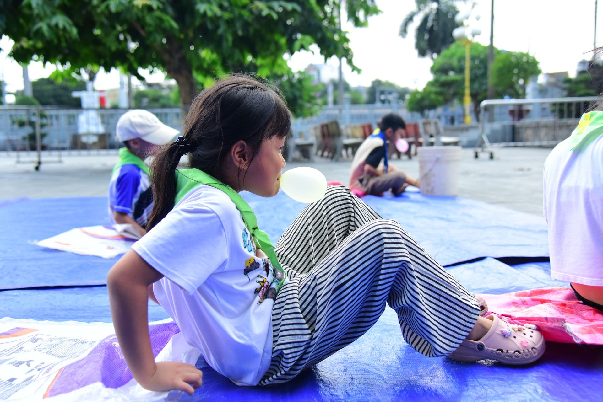 Girl in striped pants blowing a bubble gum outdoors in a recreational setting.