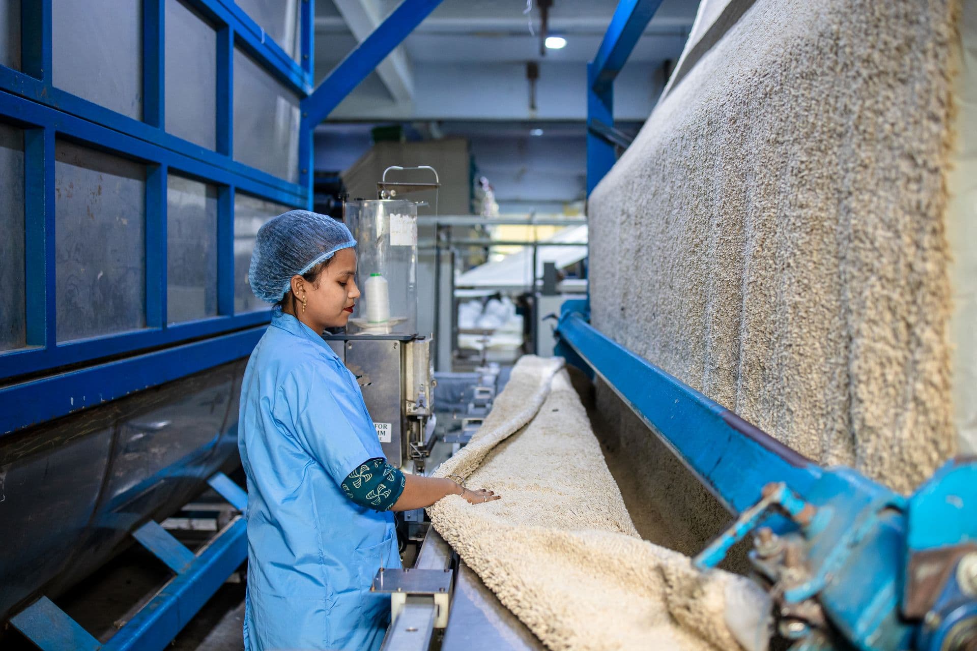 A woman in blue uniform operates machinery in a textile factory, showcasing industrial work.