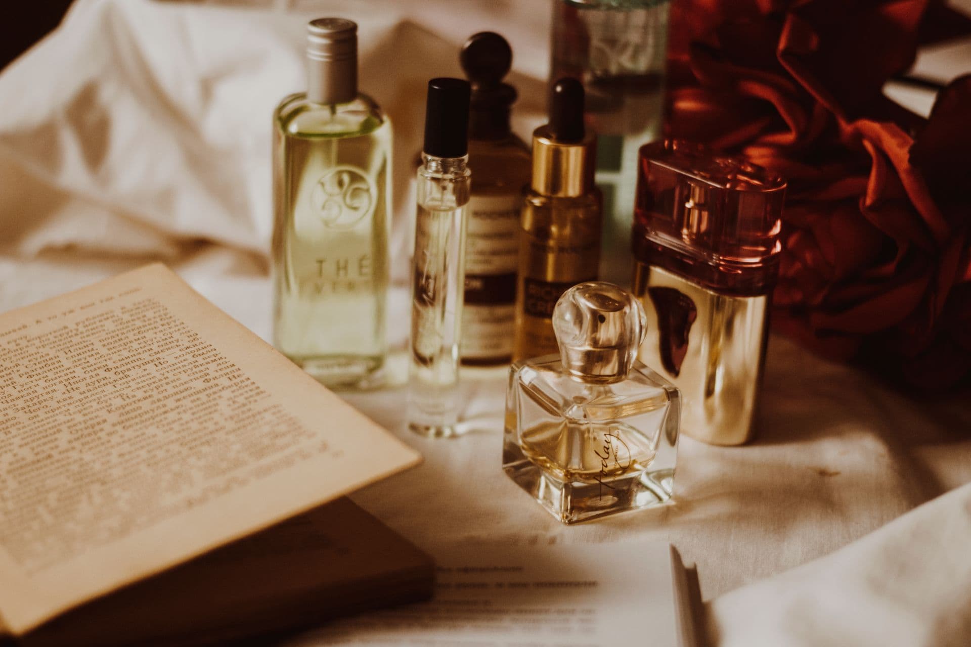 Aesthetic still life of assorted perfume bottles and an open book on a table.