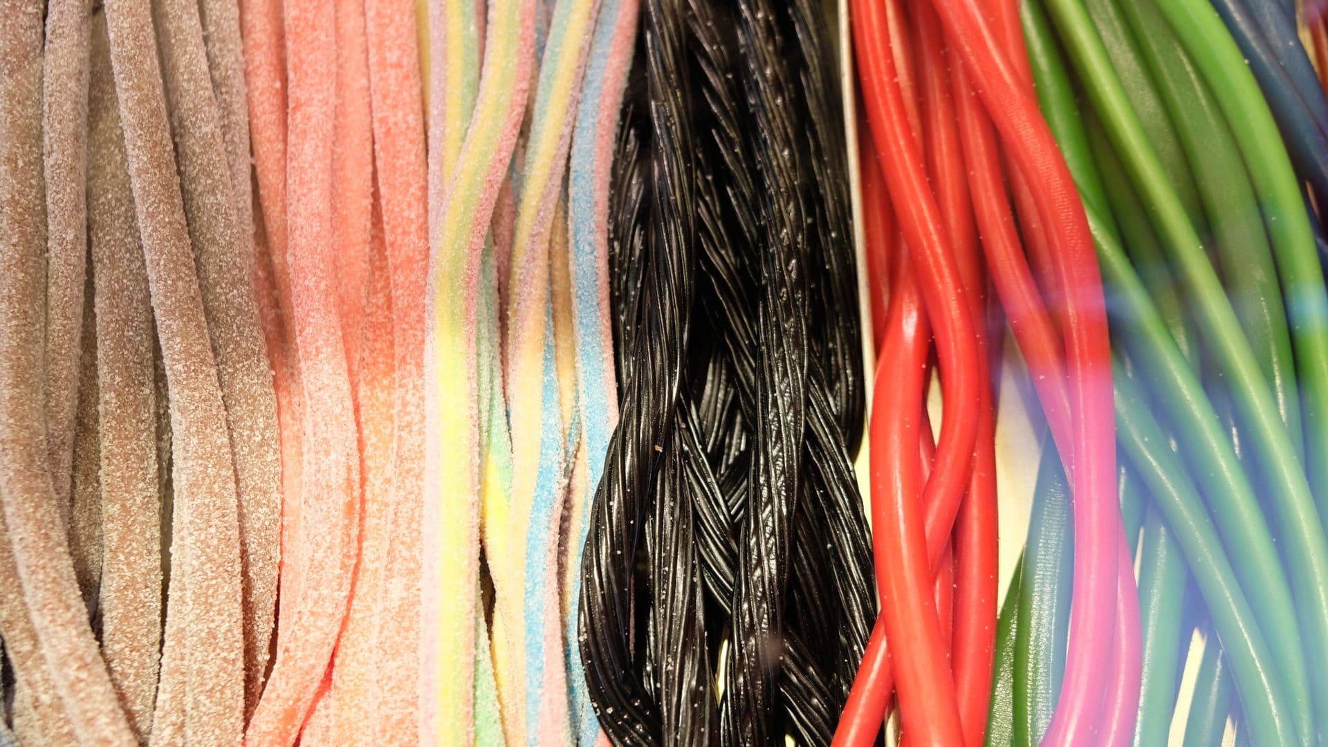 Multicolored sweet marmalade gummy sticks with sugar powder placed in row in confectionery
