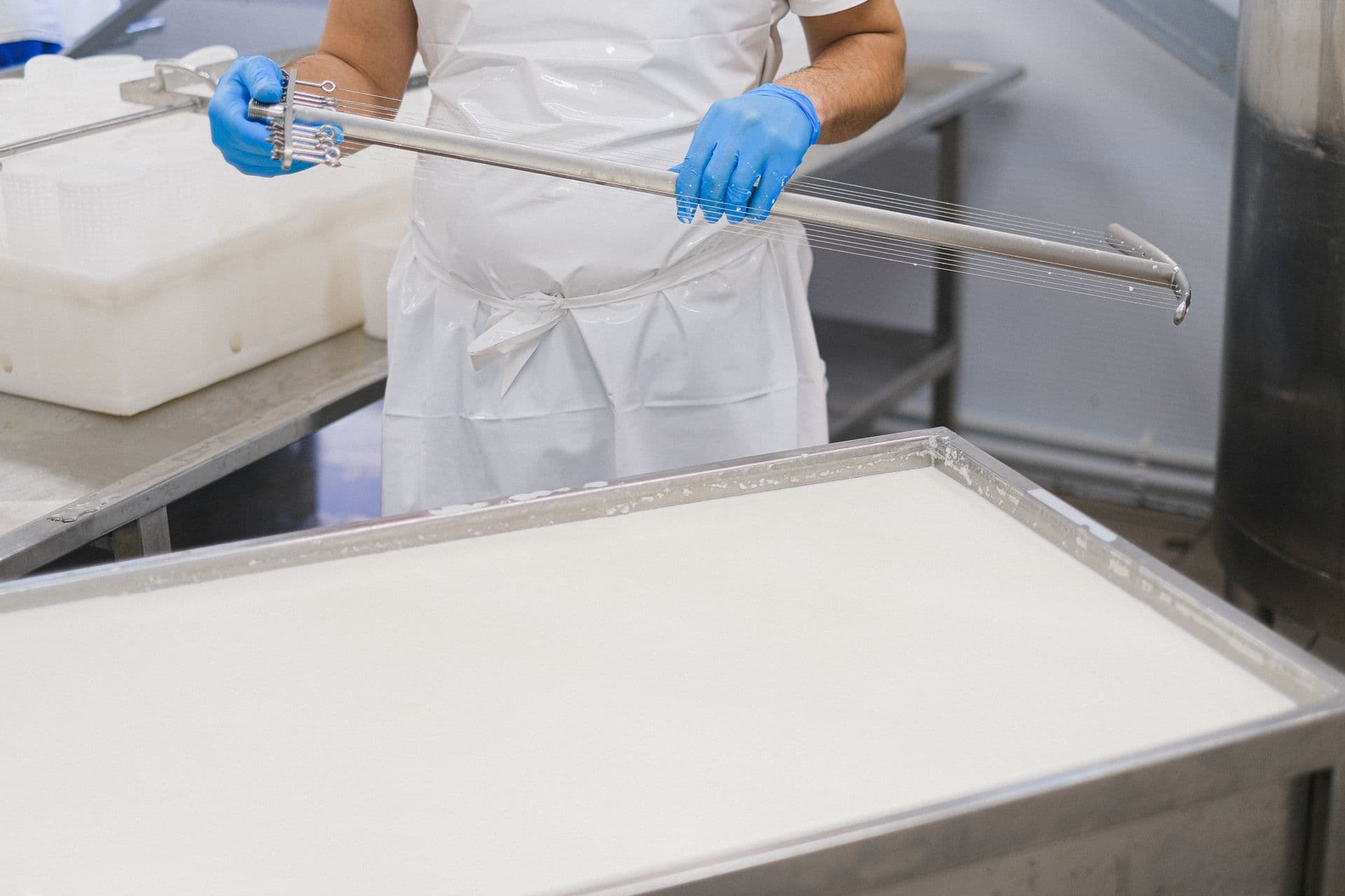 A worker using a cheesemaking tool in a factory setting, wearing protective clothing.