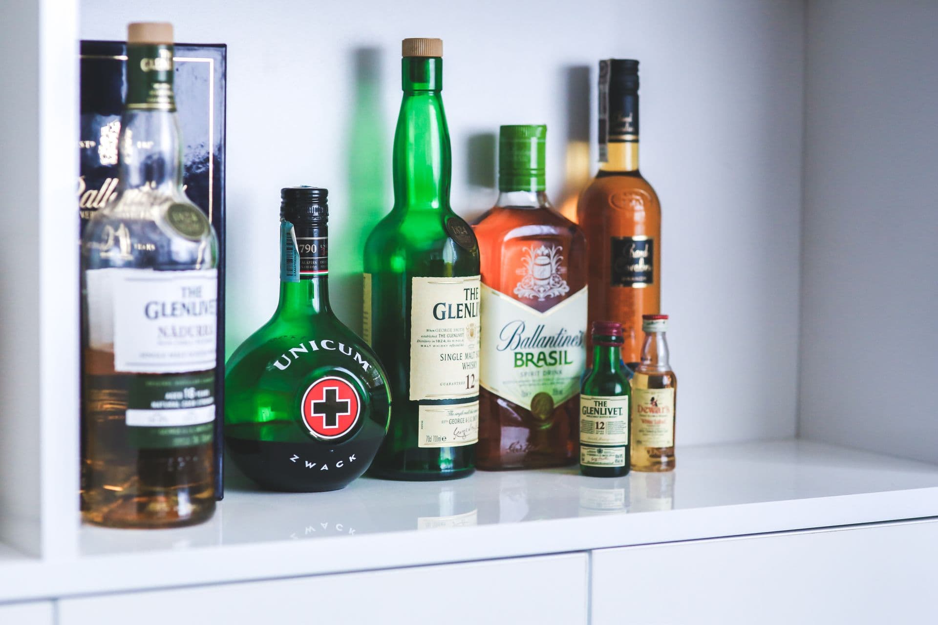 A collection of various brand liquor bottles displayed on a white shelf in a contemporary setting.