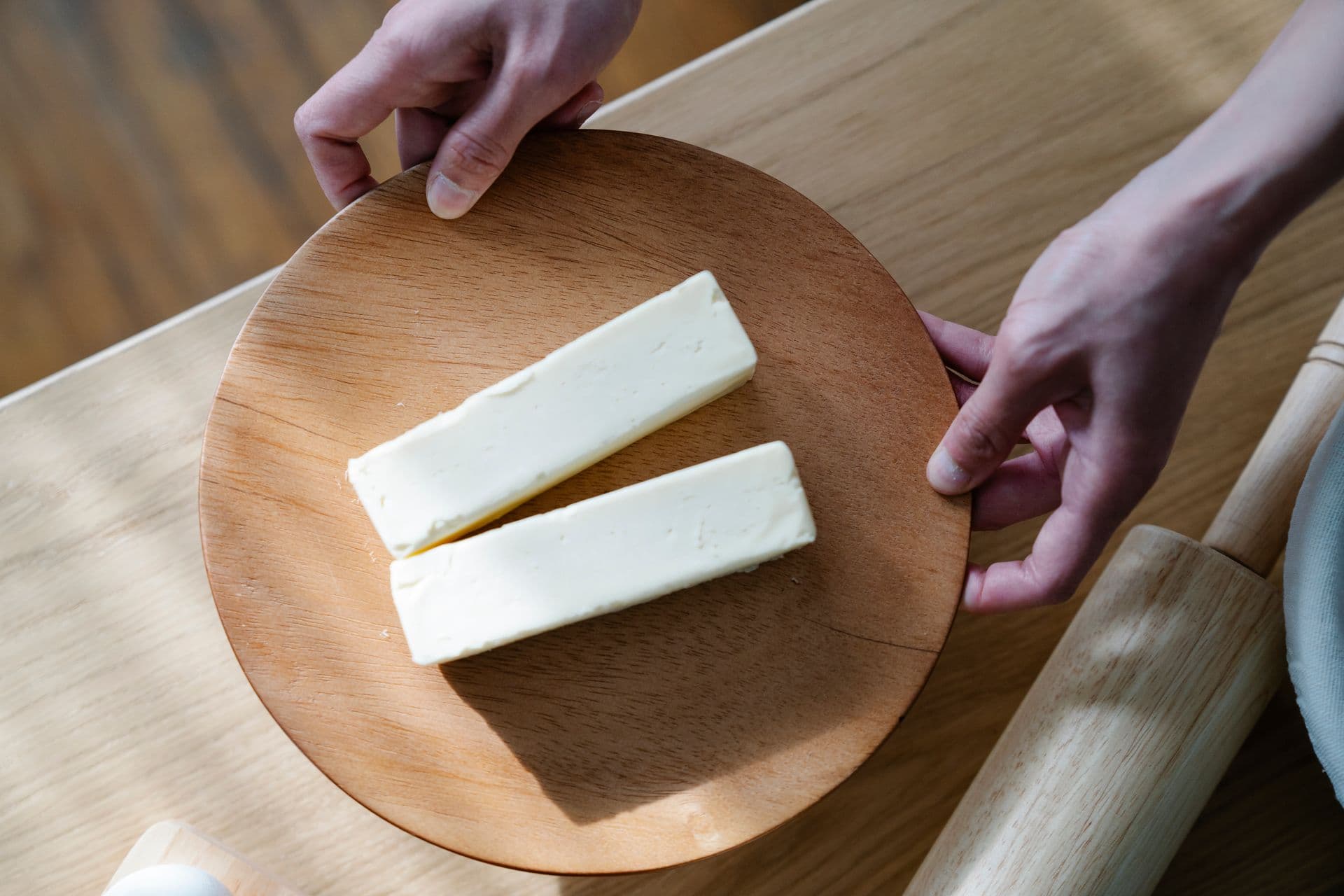 Close-up of hands holding a wooden plate with two butter sticks. Ideal for food and culinary themes.