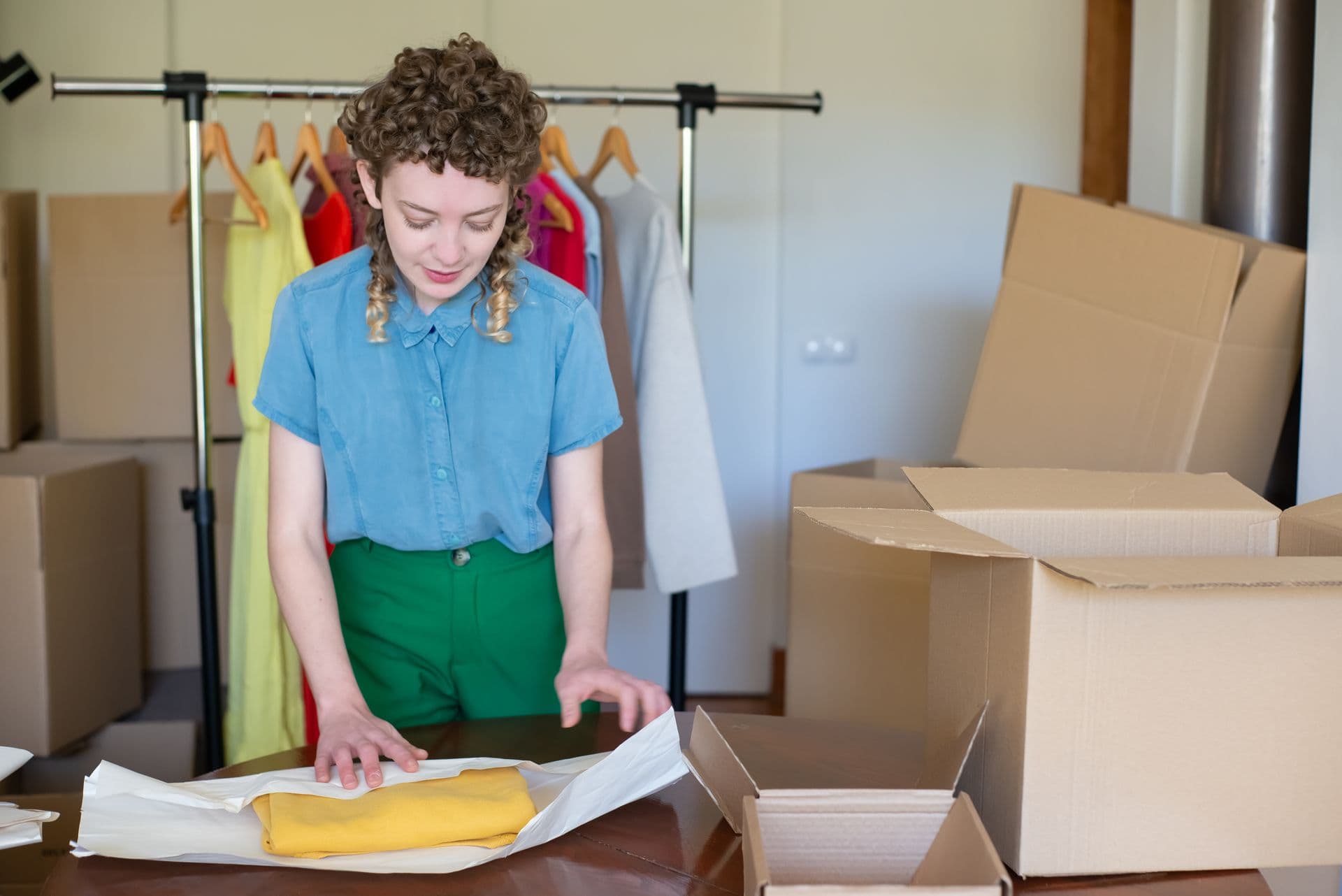 A young female entrepreneur packaging clothes in eco-friendly boxes in her online store workspace.