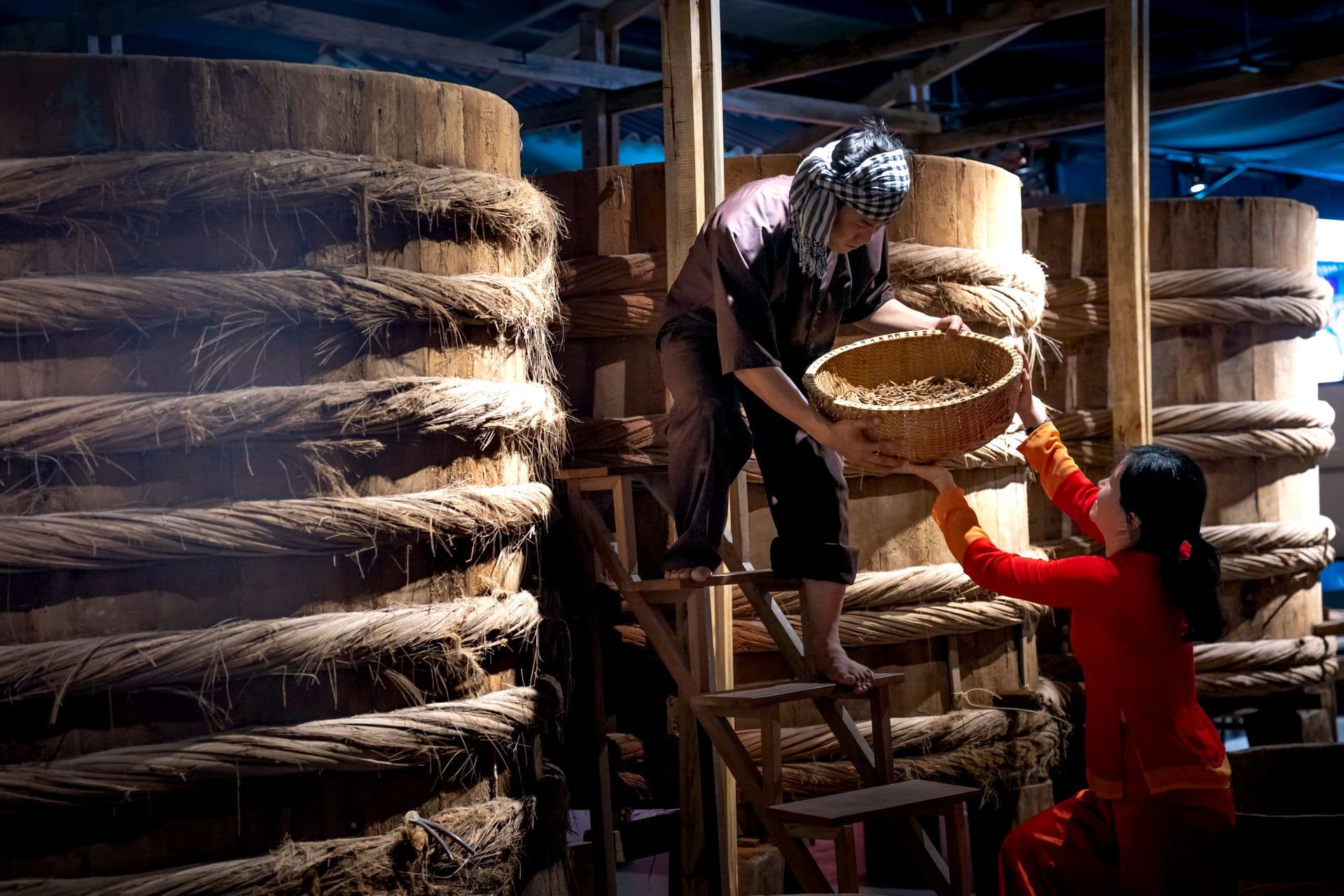 Serious ethnic male worker standing on ladder near barrels with fish sauce while working with colleague