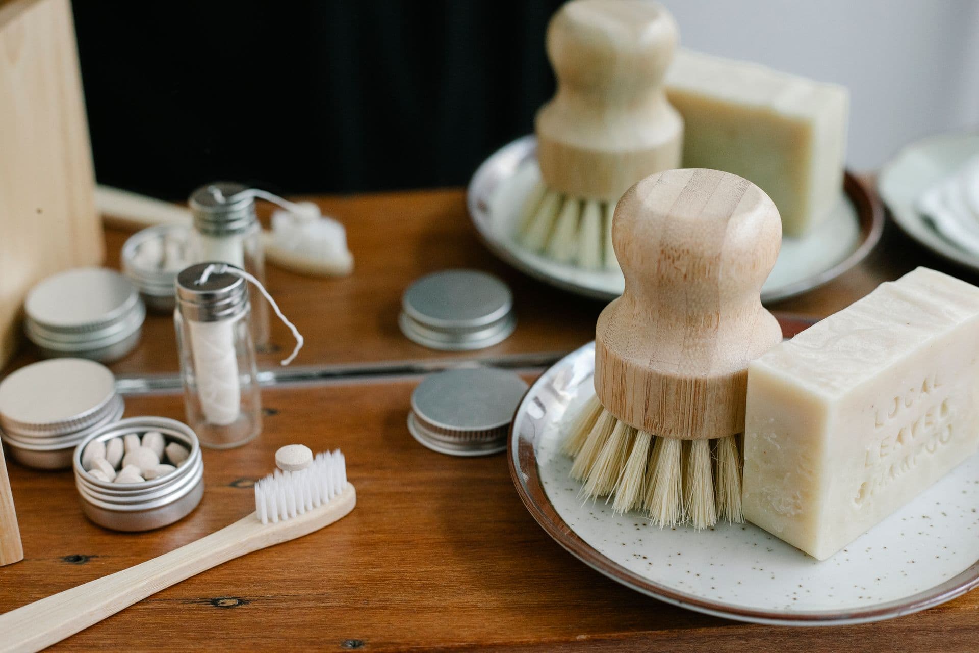 Toothbrush near toothpaste tablets placed on wooden shelf neat plate with body brush and soap near mirror in light bathroom