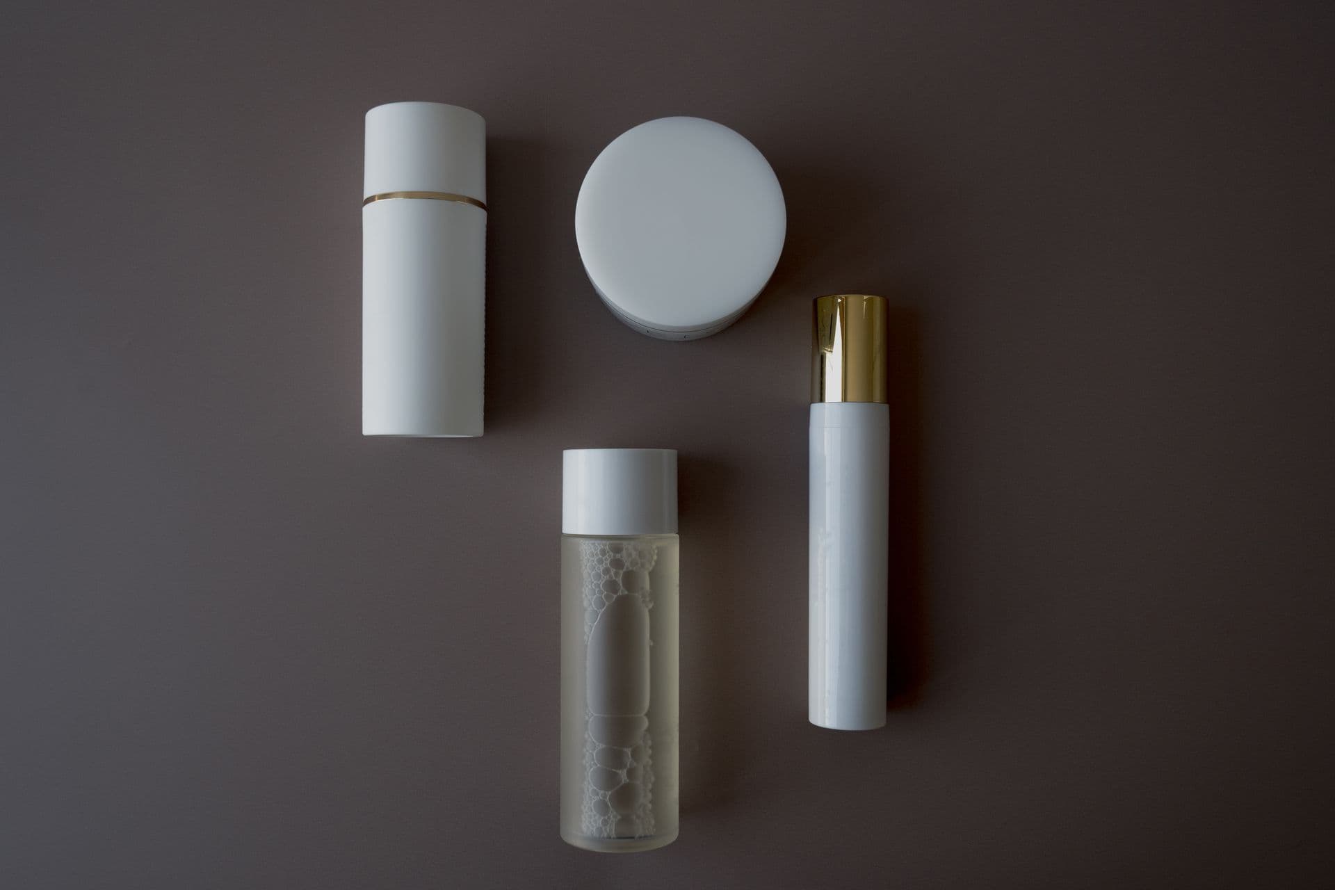 Skincare bottles and flasks arranged on a grey background, seen from above